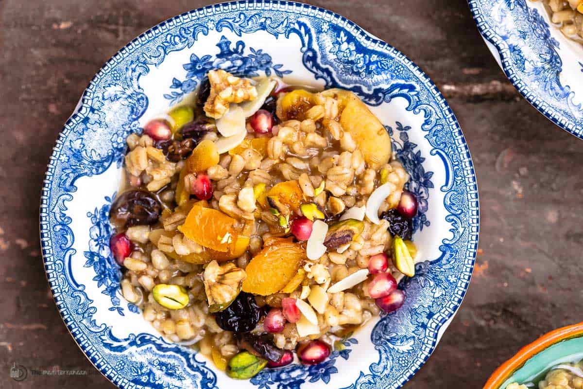 close up of burbara (wheat berry pudding) in a blue and white bowl topped with pomegranate seeds and nuts