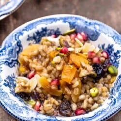 burbara (wheat berry pudding) in a bowl garnished with walnuts, pistachios, almonds, and pomegranate seeds