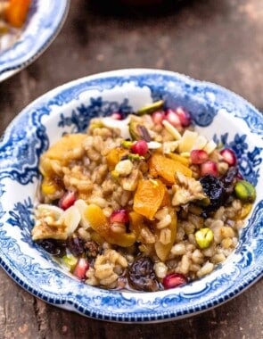 burbara (wheat berry pudding) in a bowl garnished with walnuts, pistachios, almonds, and pomegranate seeds