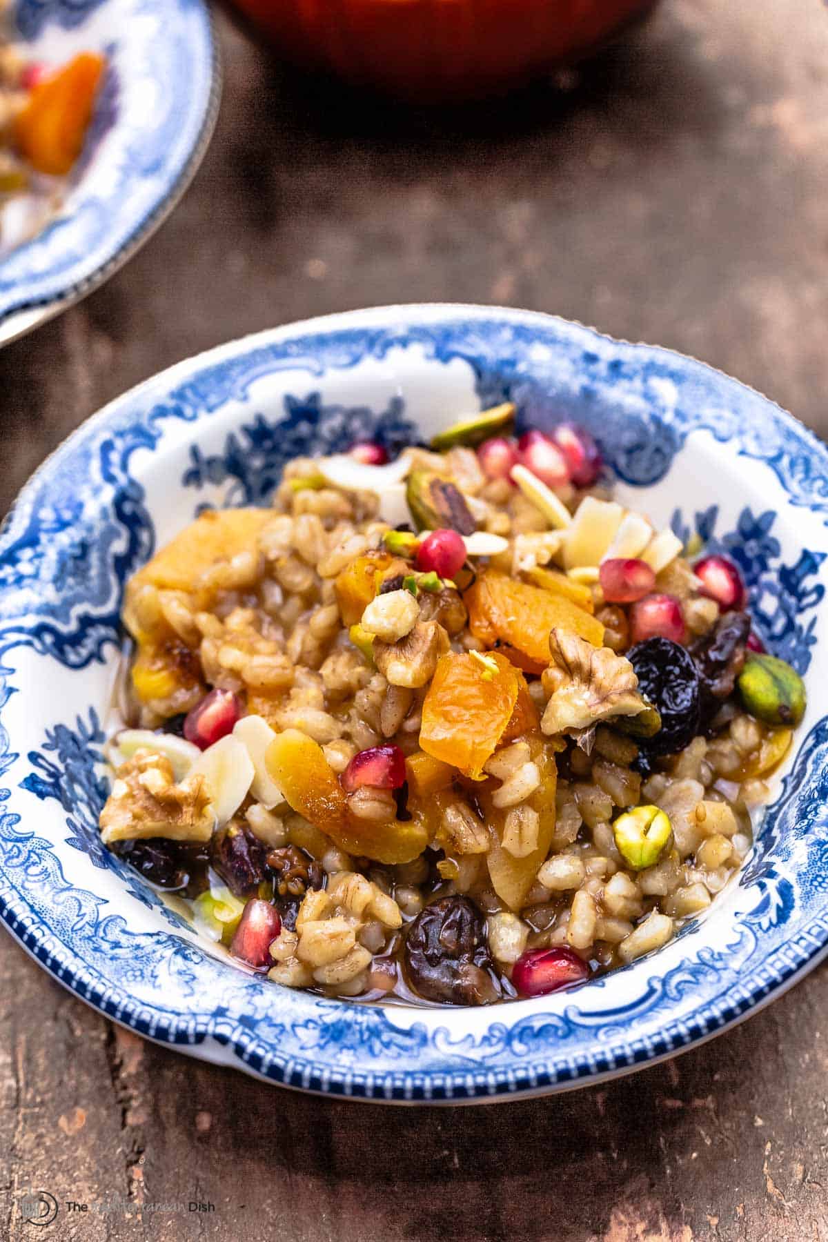 burbara (wheat berry pudding) in a bowl garnished with walnuts, pistachios, almonds, and pomegranate seeds