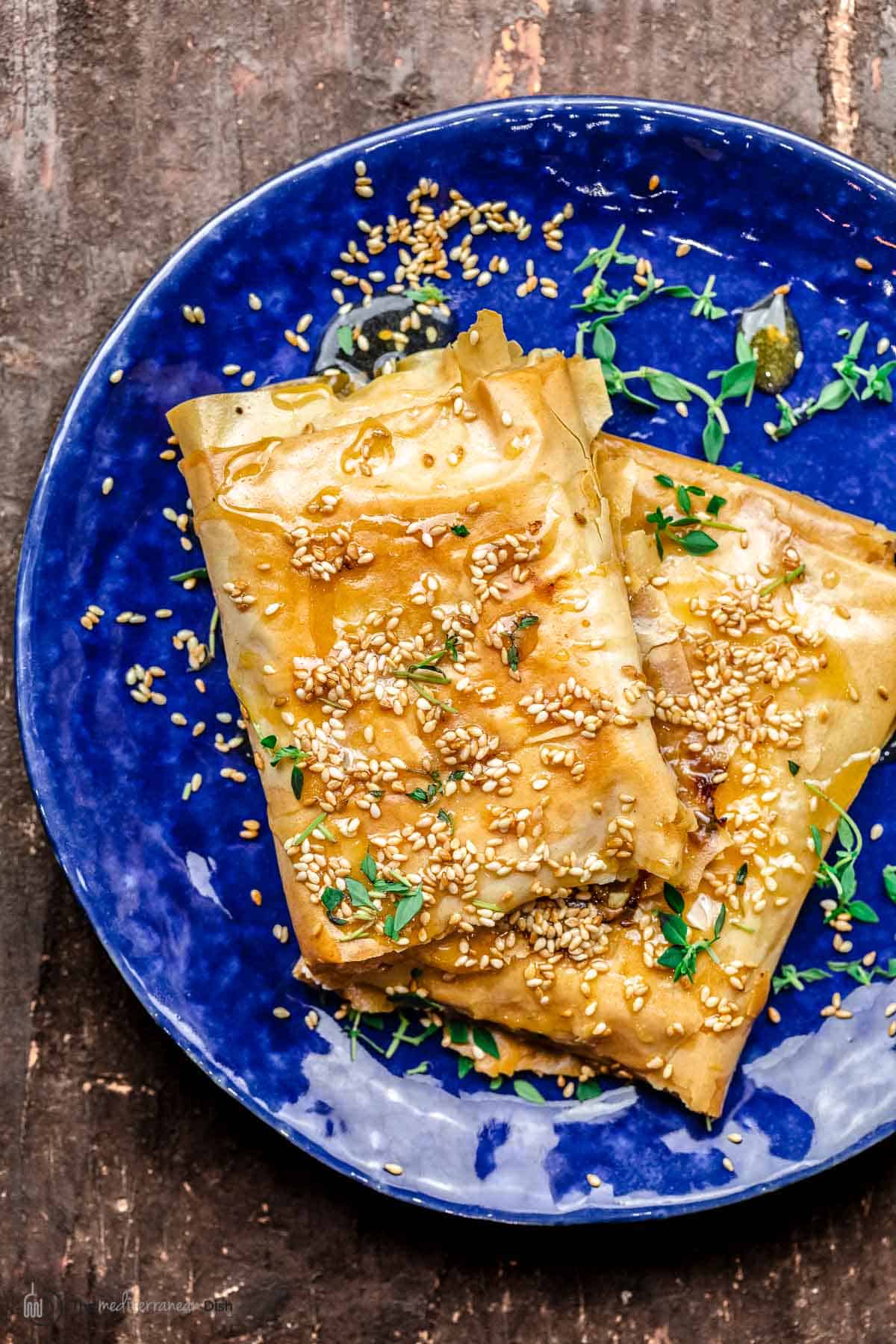 two blocks of filo-wrapped feta cheese. Topped with honey, sesame seeds, and fresh thyme