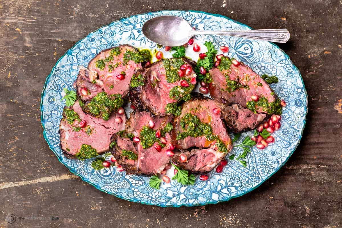 slices of slow-roasted tenderloin of beef on a platter with herby chermoula sauce and pomegranate seeds