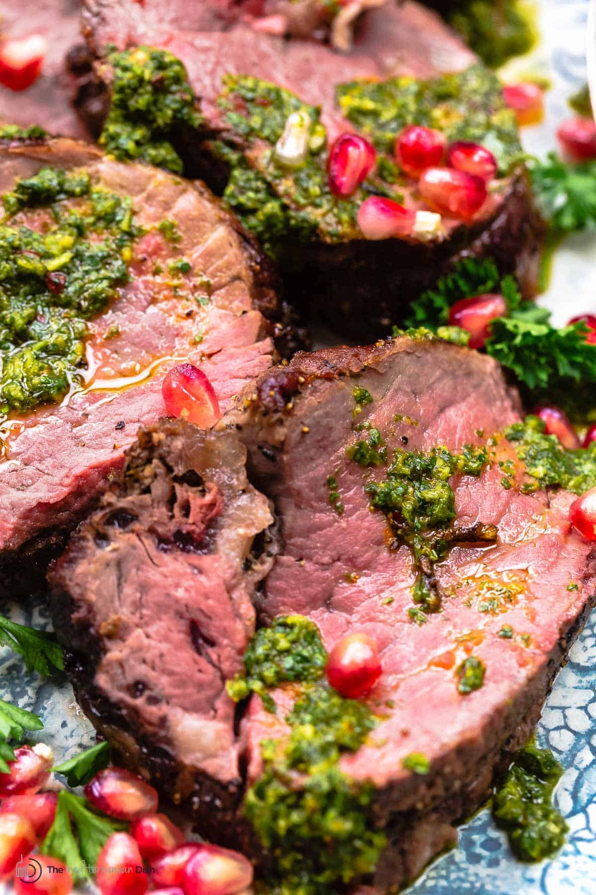 close up of sliced roasted beef tenderloin with chermoula and pomegranate seeds