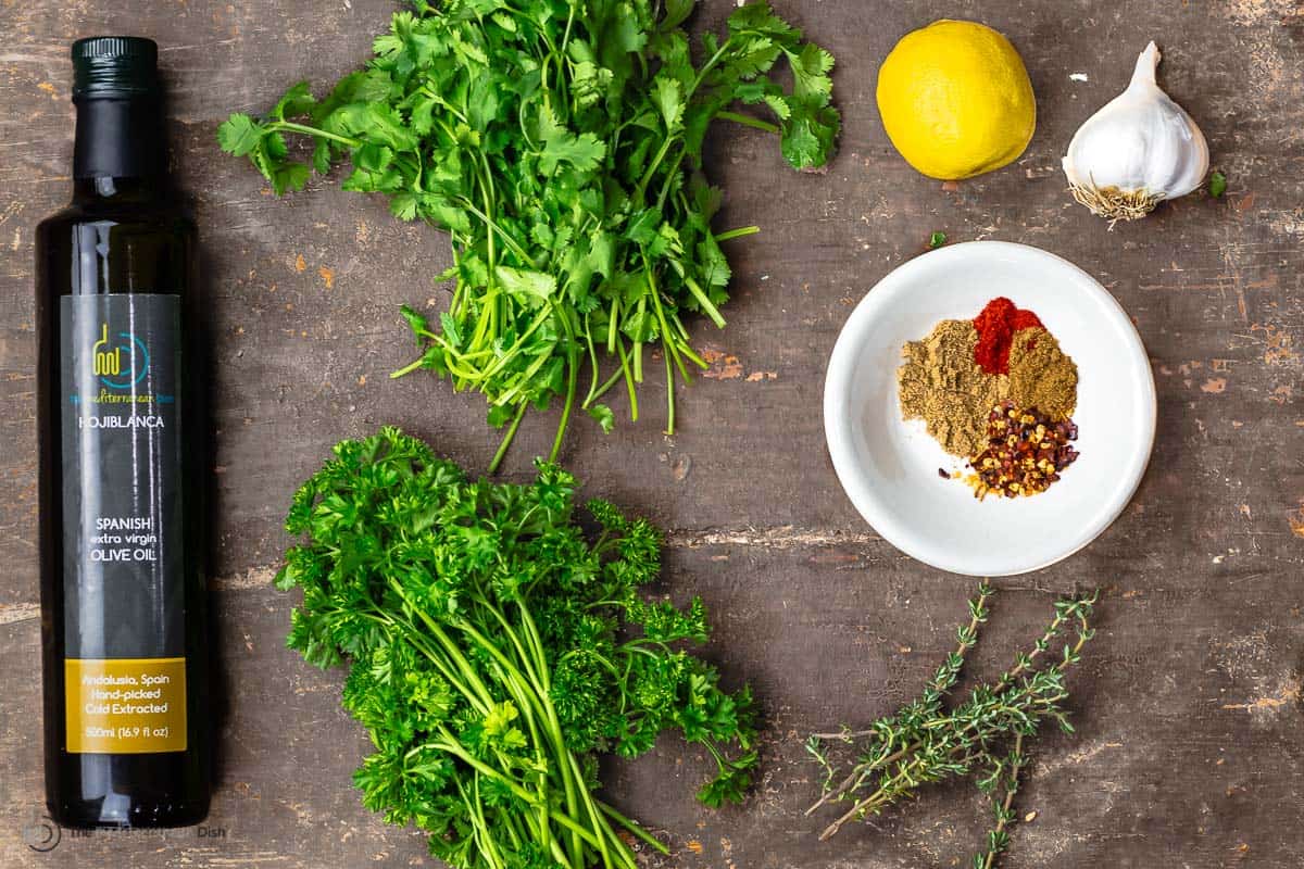 olive oil; fresh parsley and cilantro; lemon; garlic; spices on a wooden chopping board