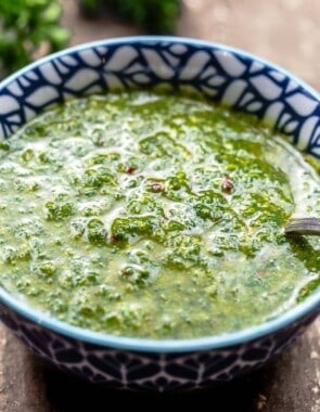 prepared chermoula in a blue and white bowl with fresh herbs in the background