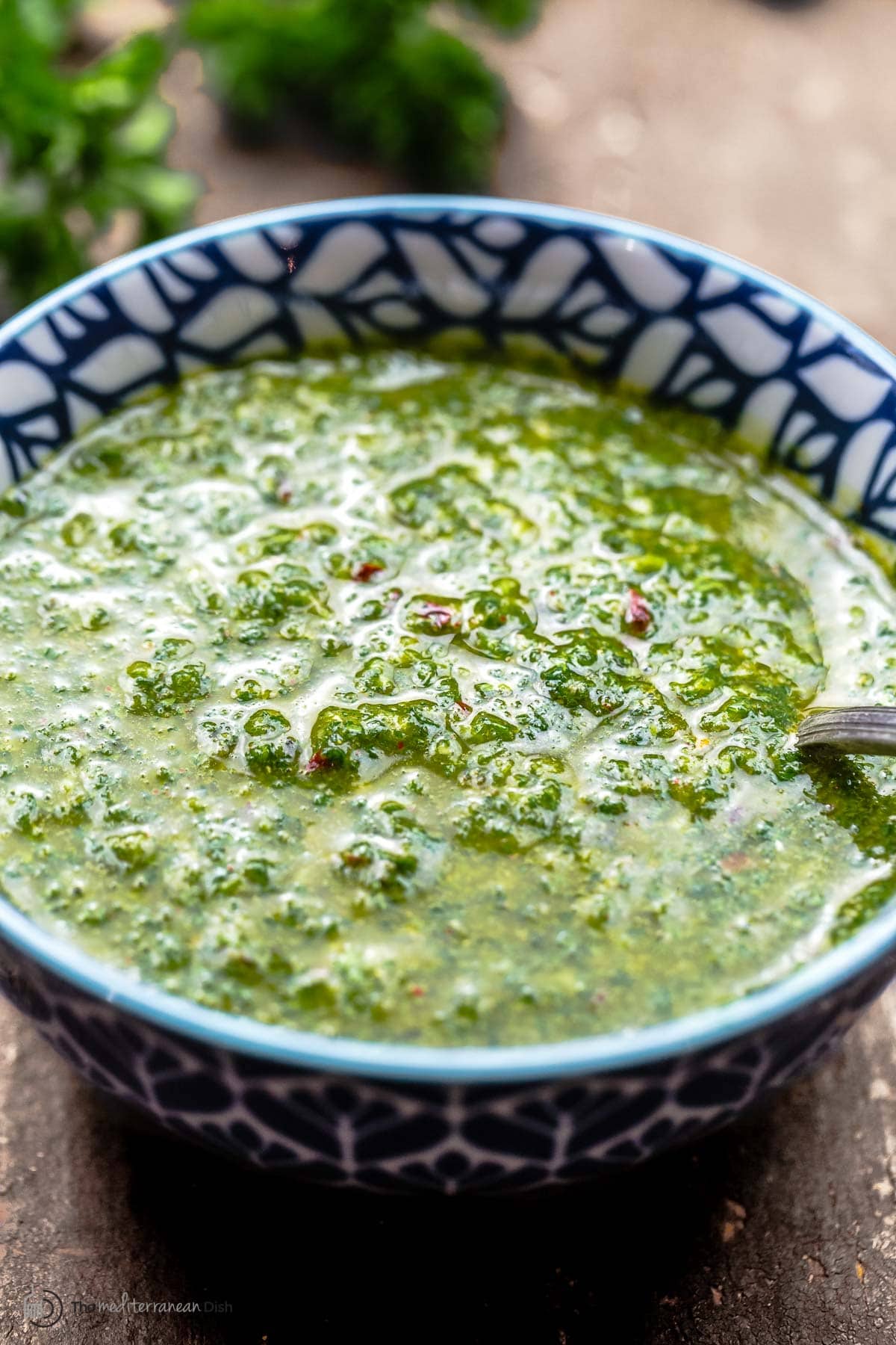 prepared chermoula in a blue and white bowl with fresh herbs in the background