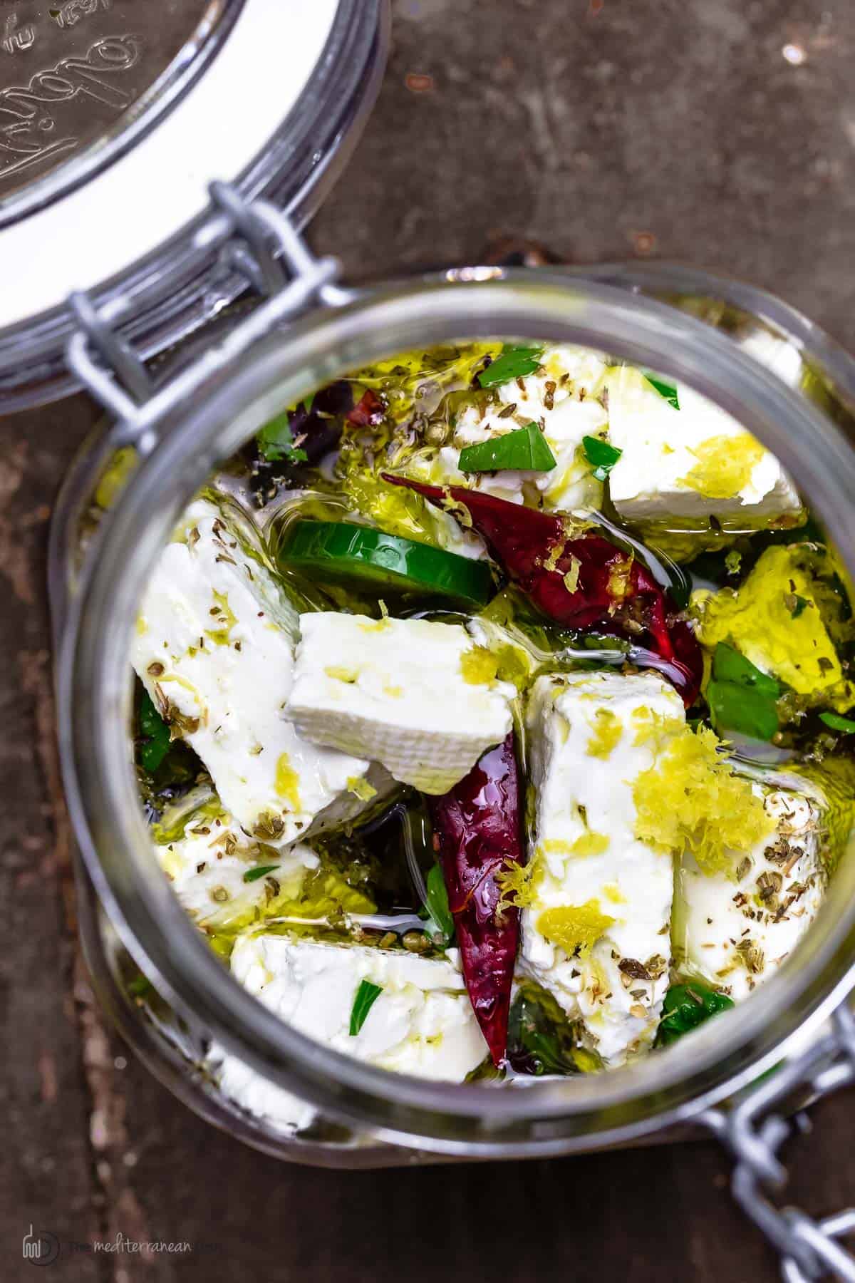 marinated feta in a jar with olive oil, dry chiles, sliced jalapeno, and orange zest