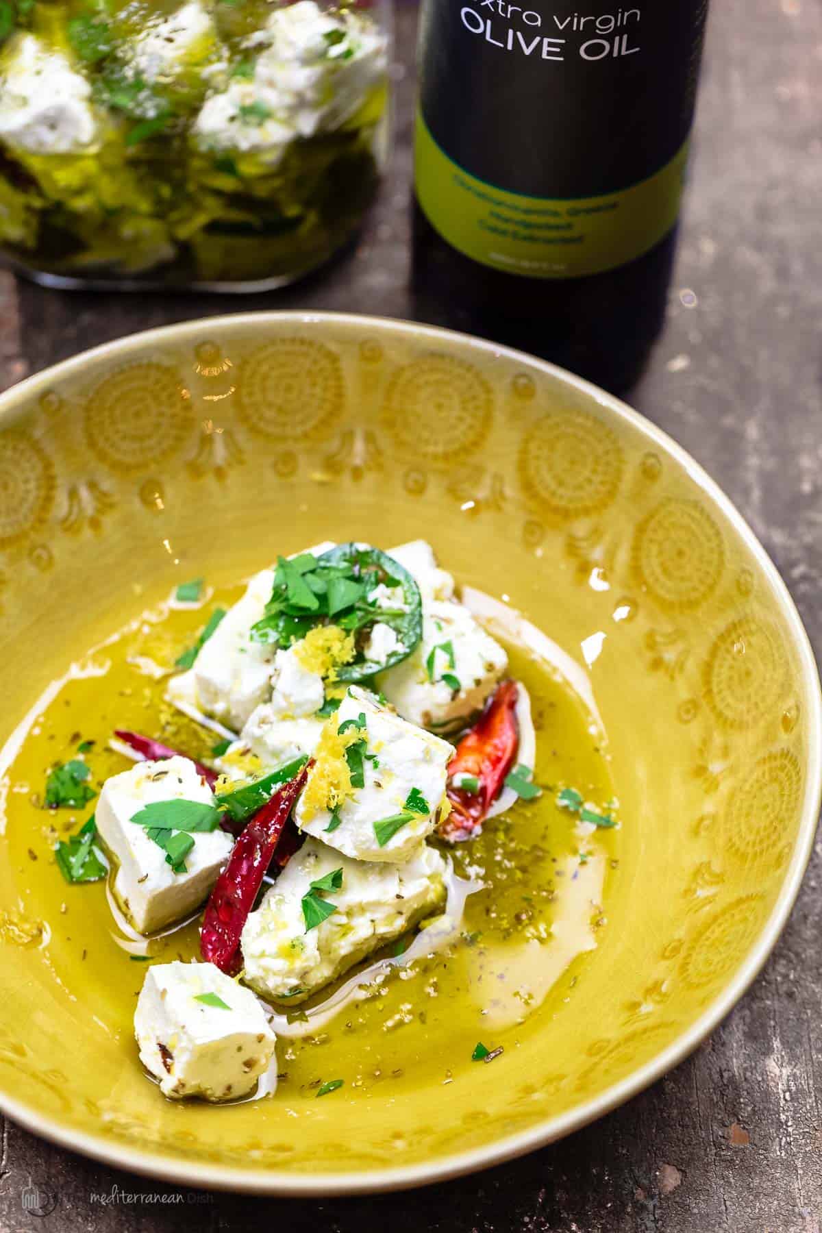 marinated feta with olive oil, dry chiles, jalapeno, orange zest, and herbs in a yellow bowl