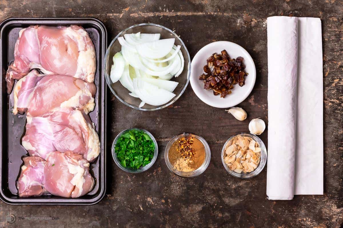 ingredients for pastilla: chicken thighs, sliced onion, chopped dates, fresh herbs, spices, garlic, toasted nuts, and phyllo dough