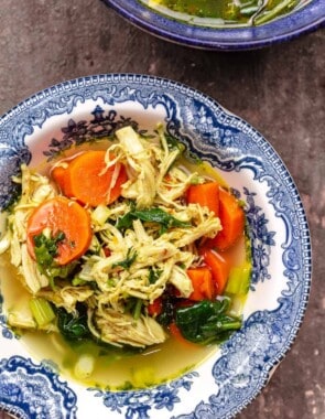 chicken soup with lemon, turmeric, carrots, spinach, and fresh herbs in a bowl