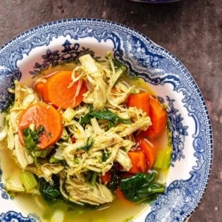 chicken soup with lemon, turmeric, carrots, spinach, and fresh herbs in a bowl