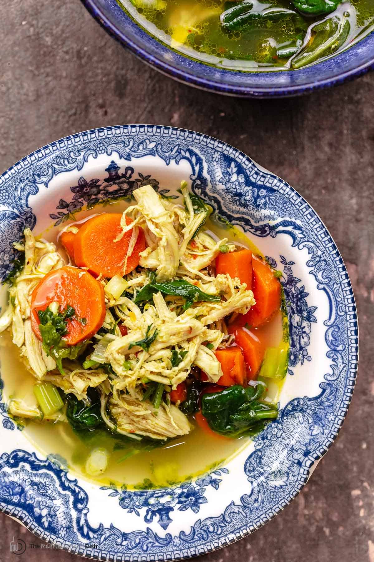 chicken soup with lemon, turmeric, carrots, spinach, and fresh herbs in a bowl