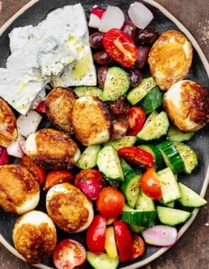 Hard boiled fried eggs on a platter with vegetables and feta cheese blocks