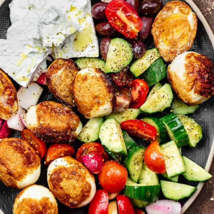 Hard boiled fried eggs on a platter with vegetables and feta cheese blocks