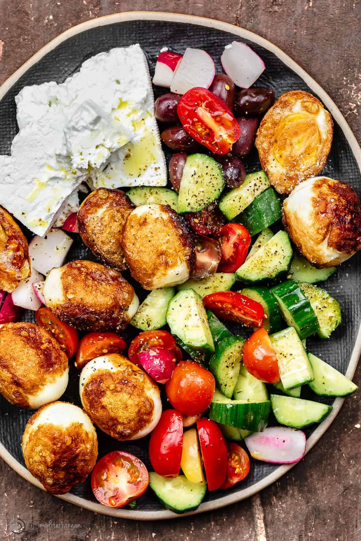 Hard boiled fried eggs on a platter with vegetables and feta cheese blocks