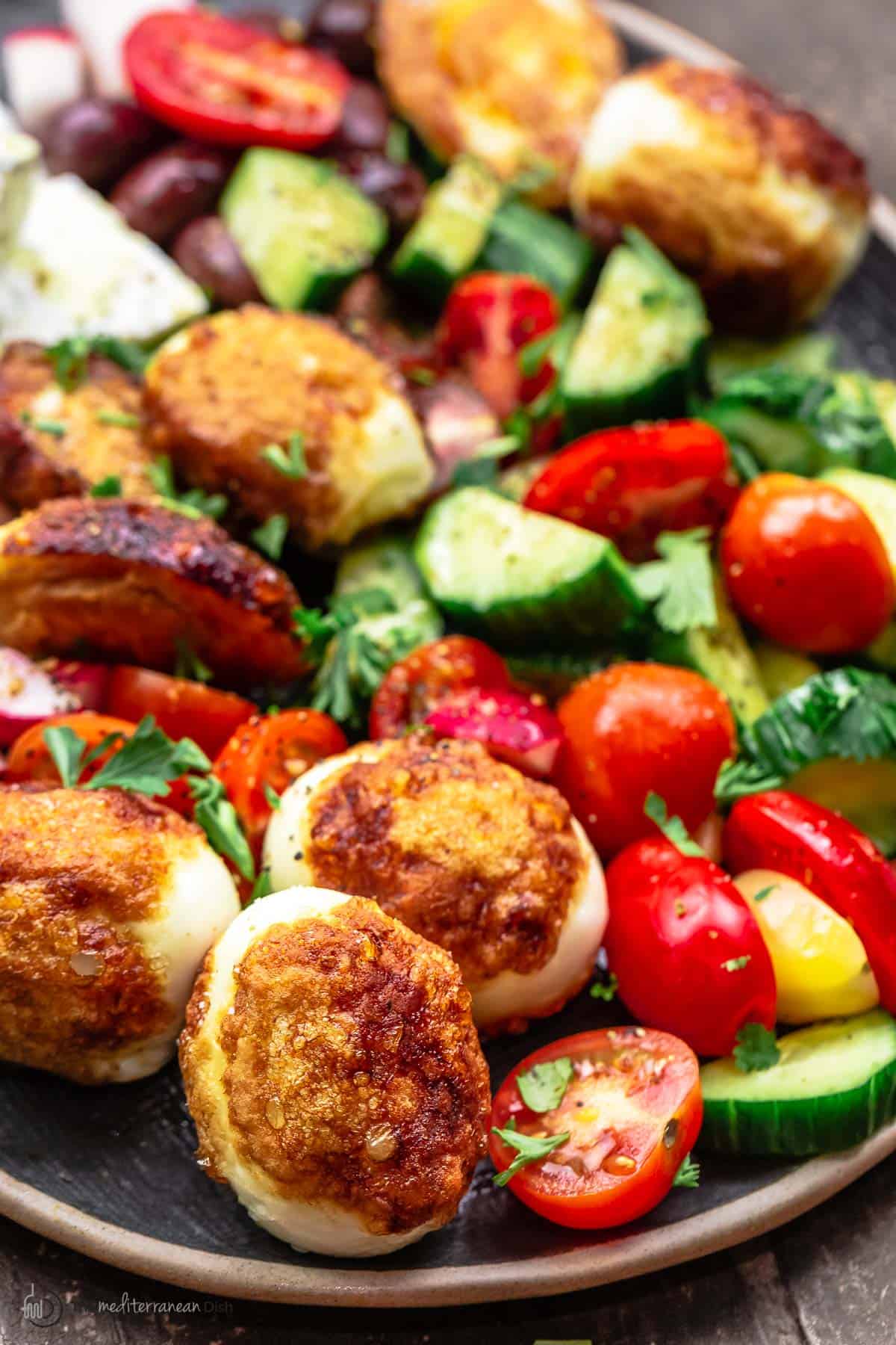 Egyptian fried boiled eggs (beid meza'lil) on a platter with tomatoes, cucumbers, and feta cheese