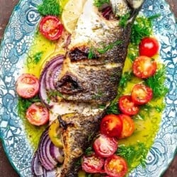 whole broiled branzino with ladolemono, cherry tomatoes, and dill on a platter