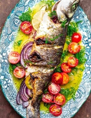 whole broiled branzino with ladolemono, cherry tomatoes, and dill on a platter