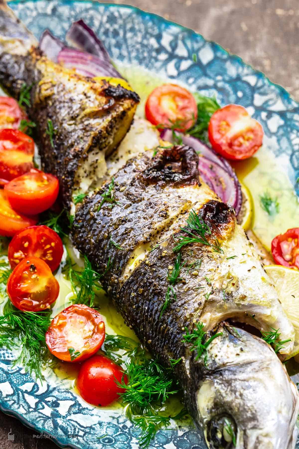 closeup of broiled branzino with ladolemono, cherry tomatoes, and dill