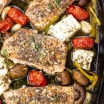 baked salmon with vegetables and slices of feta in a black baking dish