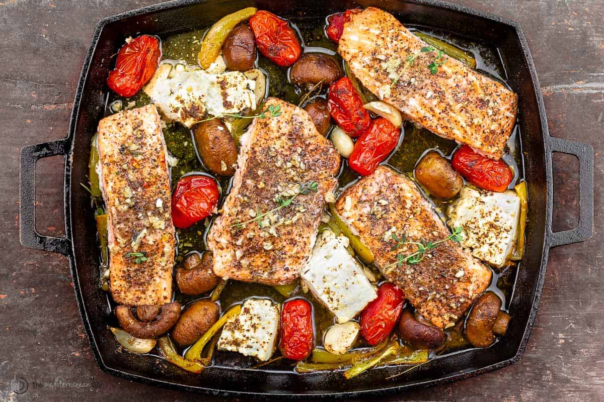 seasoned salmon, mushrooms, bell peppers, cherry tomatoes, and feta cheese in a baking dish with herbs and spices