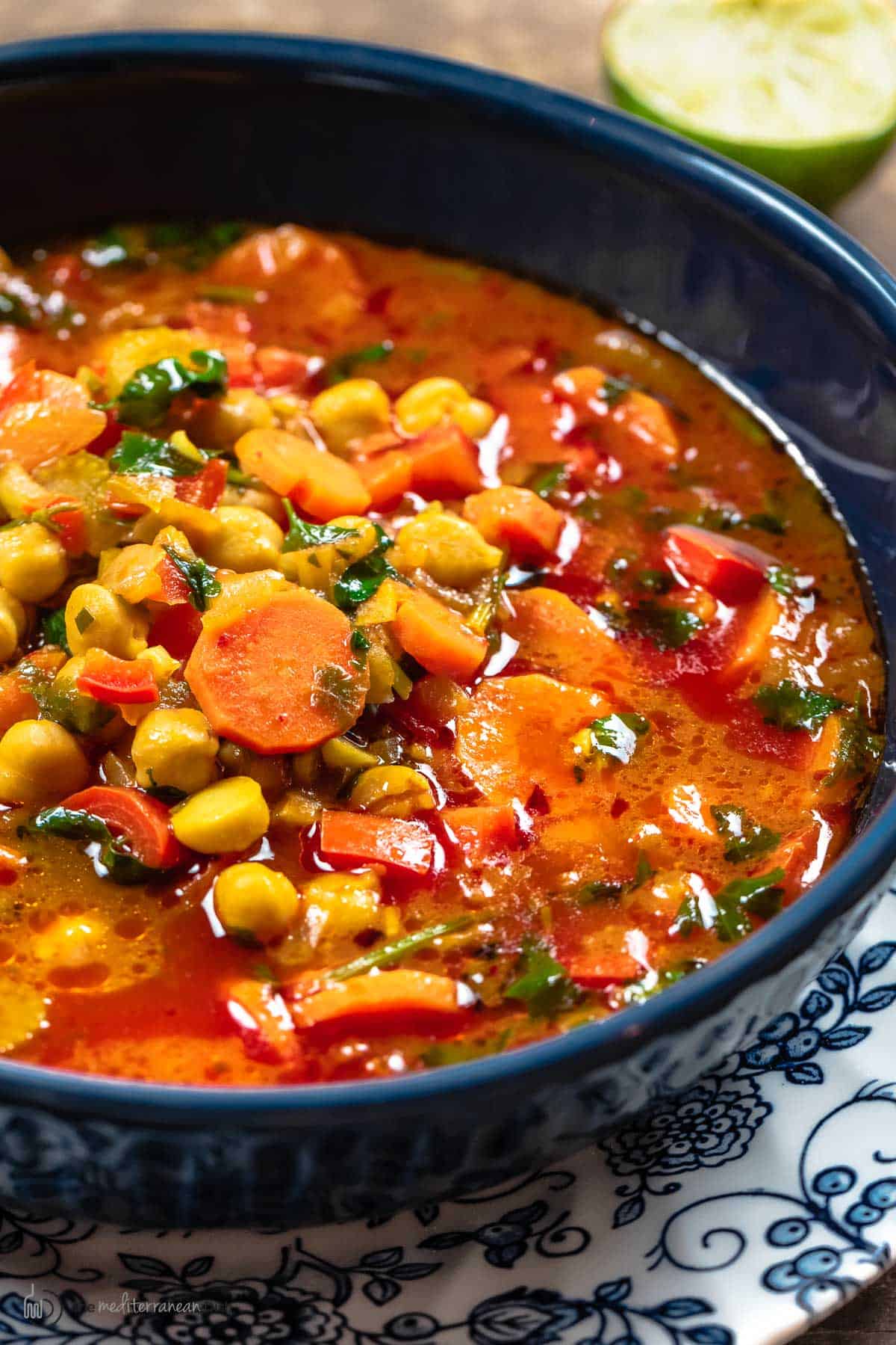 close up of vegan chickpea soup with tomatoes and vegetables in a bowl with a lime on the side