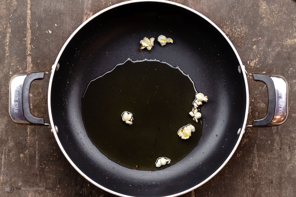 olive oil in a skillet with a few popped popcorn kernels
