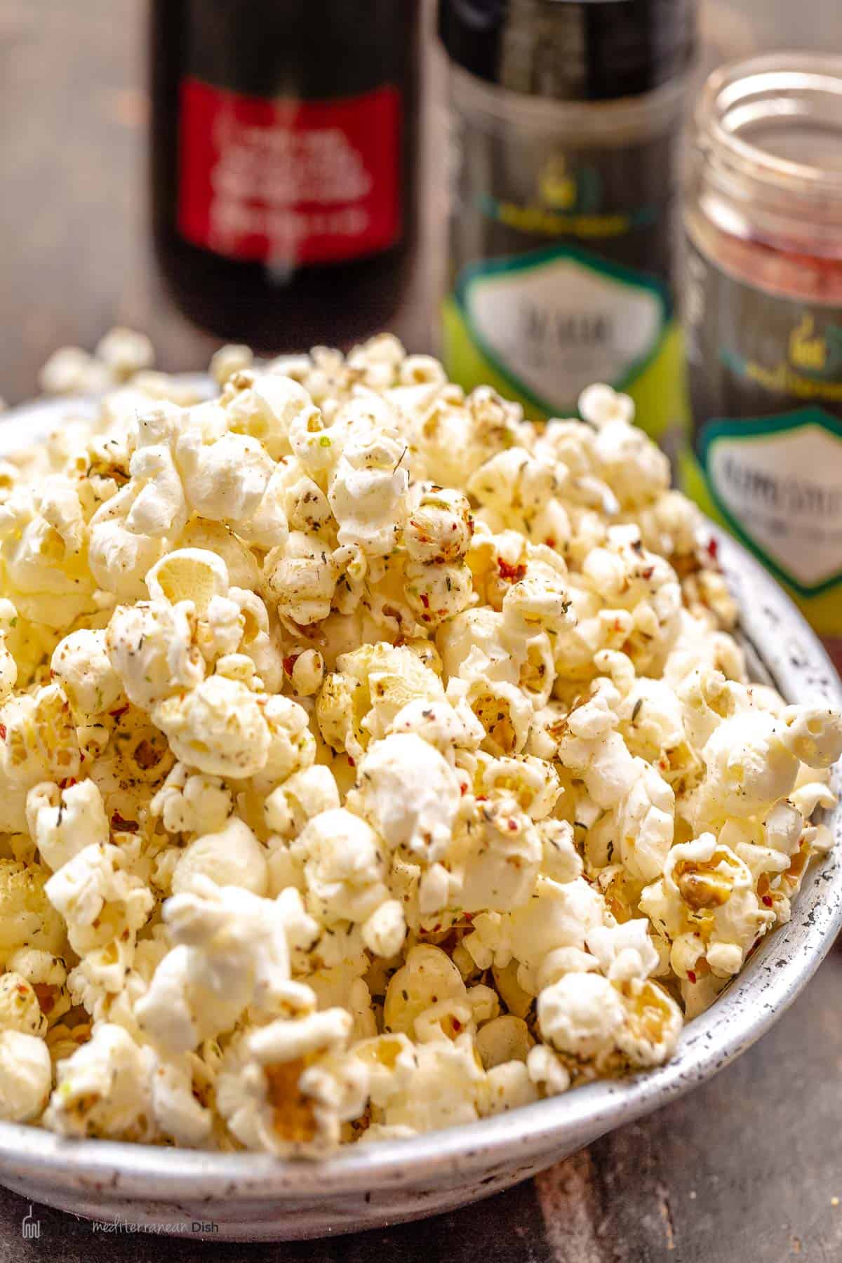 homemade popcorn in a bowl with seasonings and extra virgin olive oil in the background