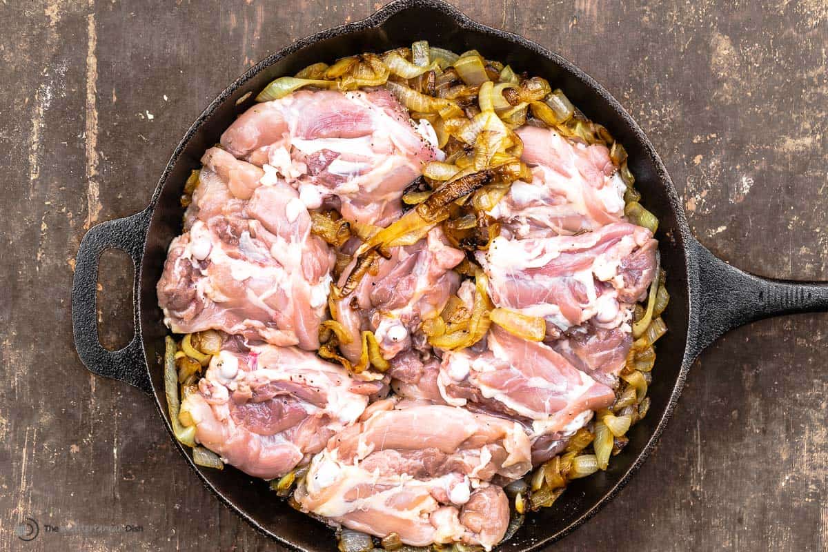 Raw skinless chicken thighs added in a cast iron skillet with caramelized onions