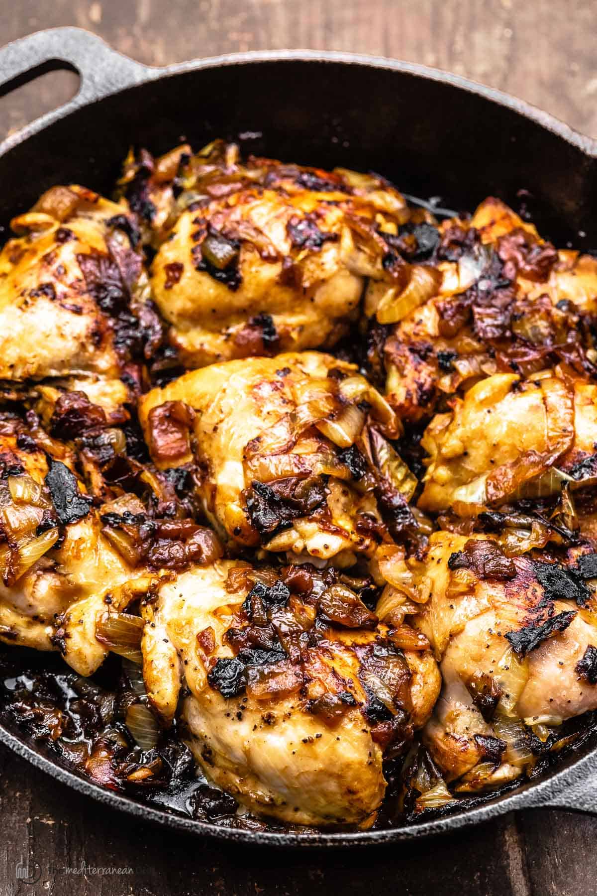 Chicken thighs and caramelized onions in a cast iron skillet, a side angle shot