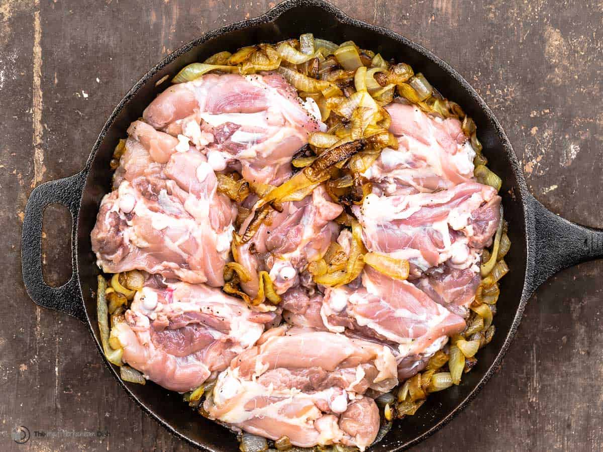 Raw skinless chicken thighs added in a cast iron skillet with caramelized onions