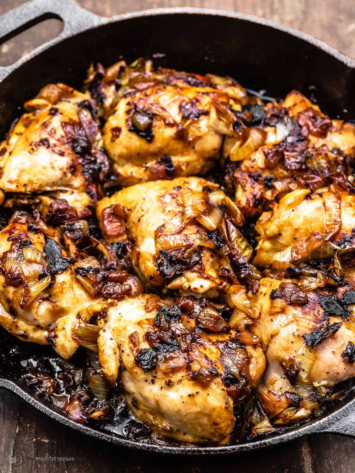 Chicken thighs and caramelized onions in a cast iron skillet, a side angle shot