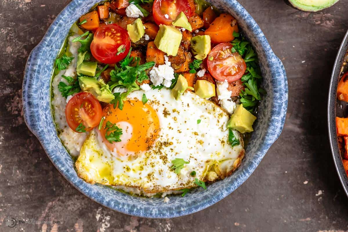 savory oats breakfast bowl with cherry tomatoes, avocado, parsley, feta cheese, and za'atar