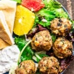 Baked turkey meatballs served on a blue plate over a salad with a side of tzatziki sauce and pita bread