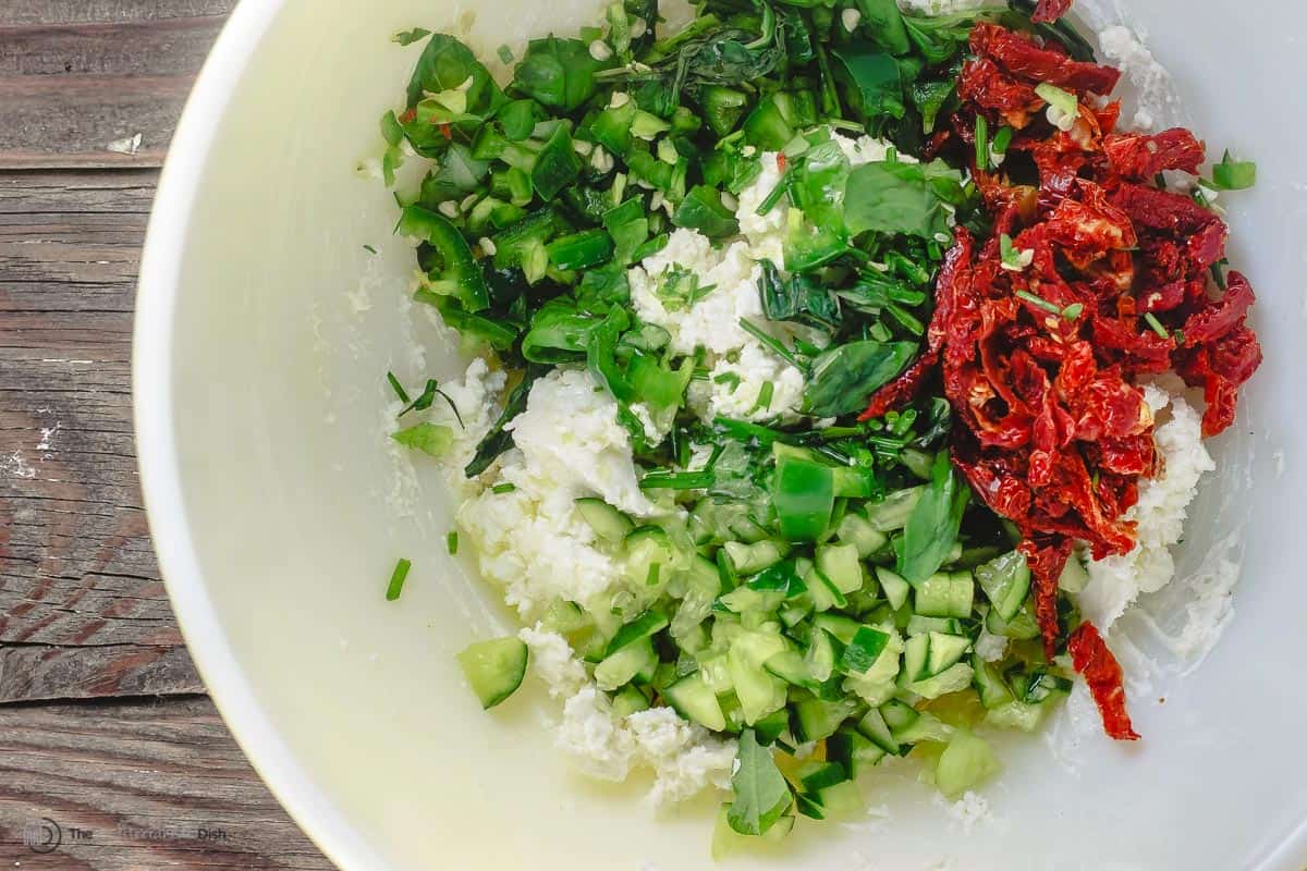 all feta dip ingredients in a bowl (cheeses, sun-dried tomato, cucumber, jalapeÃ±o, basil, and chives)