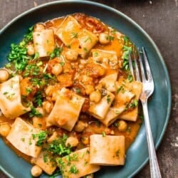 A bowl of creamy tomato pasta with chickpeas, garnished with parsley. Another bowl to the side