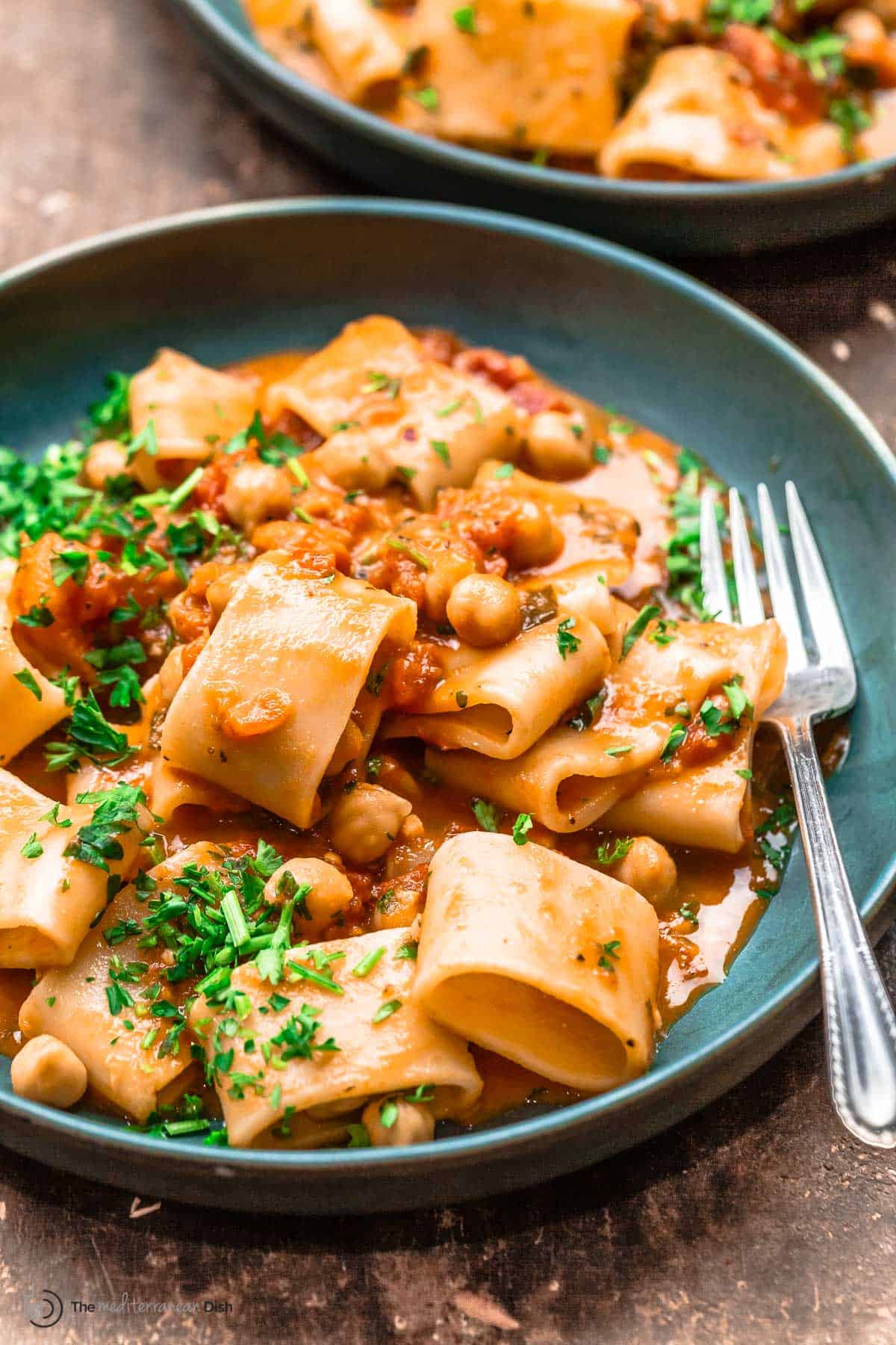 Two bowls of creamy tomato pasta with chickpeas in pink tomato sauce with parsley garnish