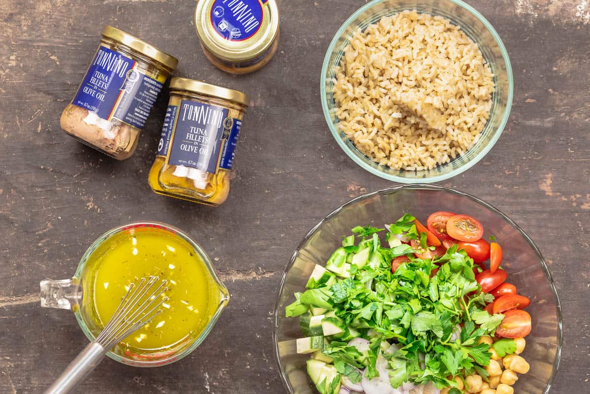 ingredients to make rice bowls with tuna, including tuna jars, greek dressing, brown rice, and Mediterranean salad
