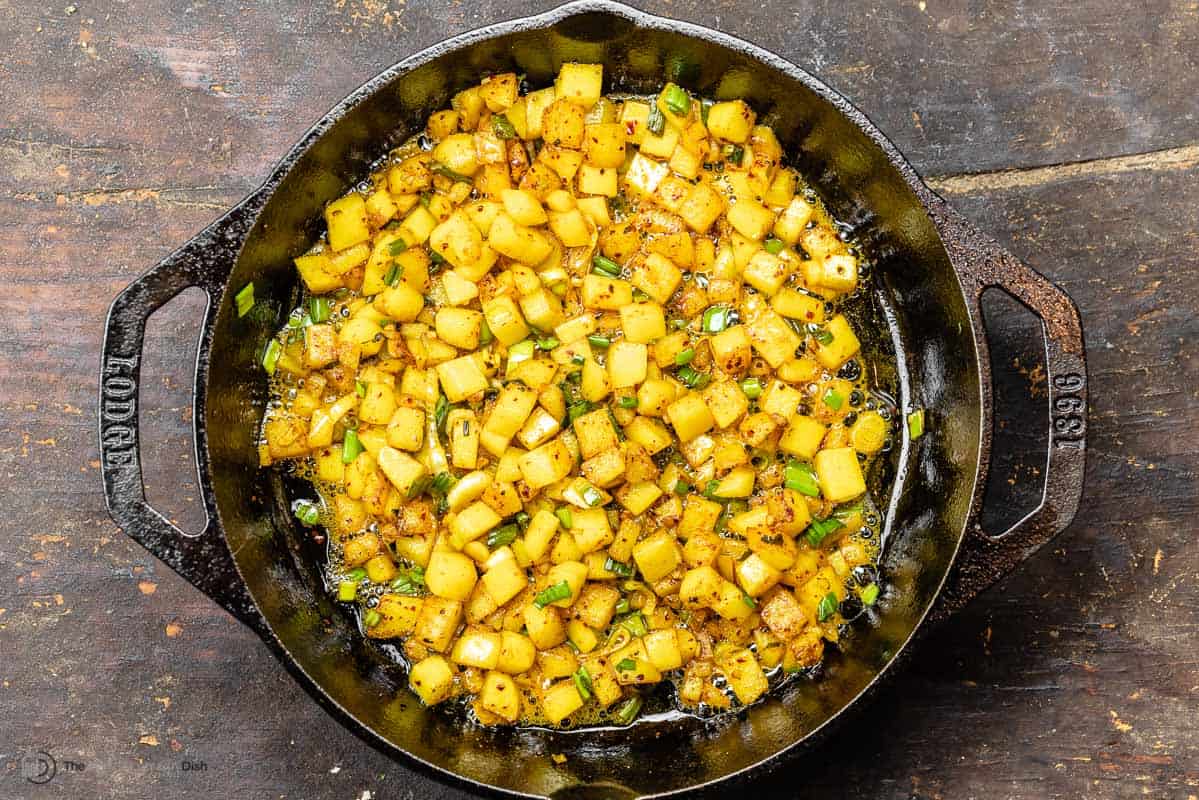 cubed potatoes cooking in a skillet with spices and aromatics