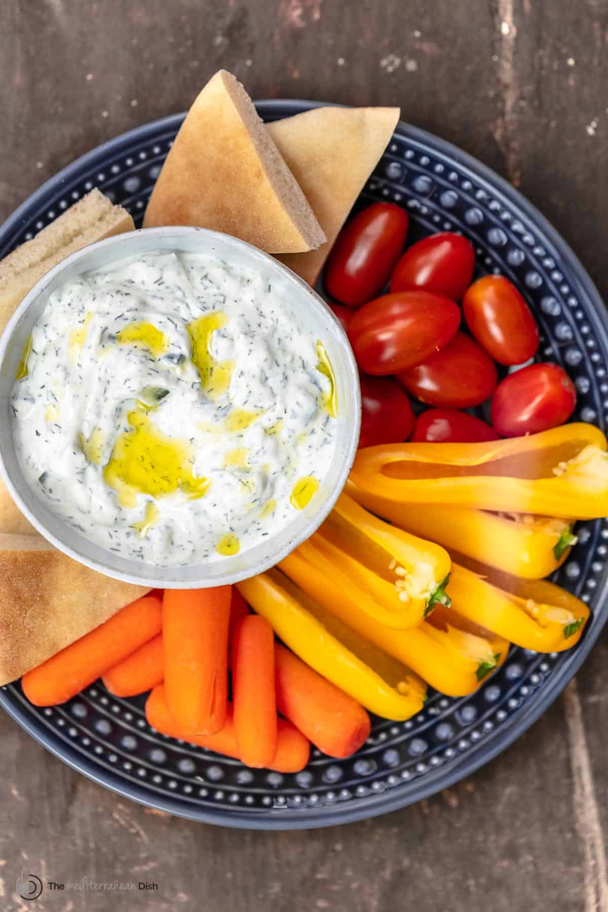 Tzatziki sauce with vegetables and pita wedges on a platter