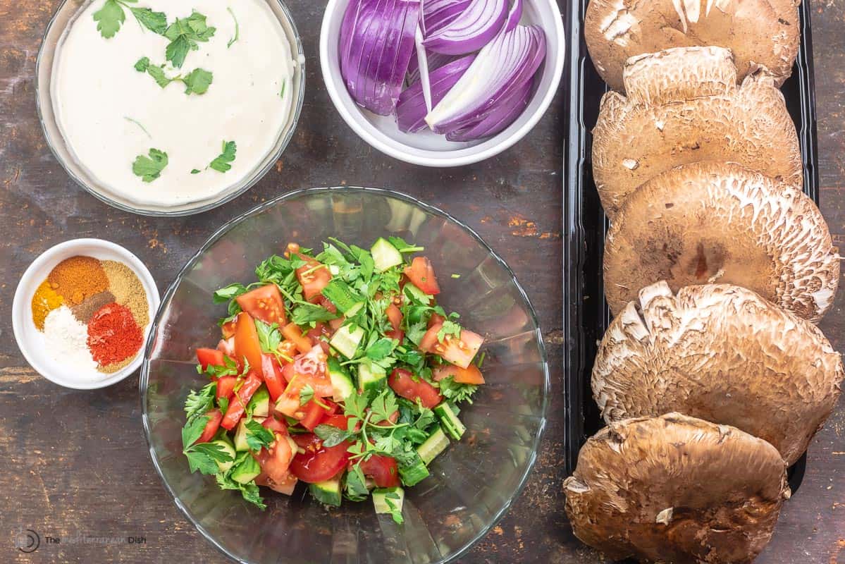 ingedients for mushroom shawarma including portobello caps, red onion, tahini sauce, Mediterranean salad, and shawarma seasoning