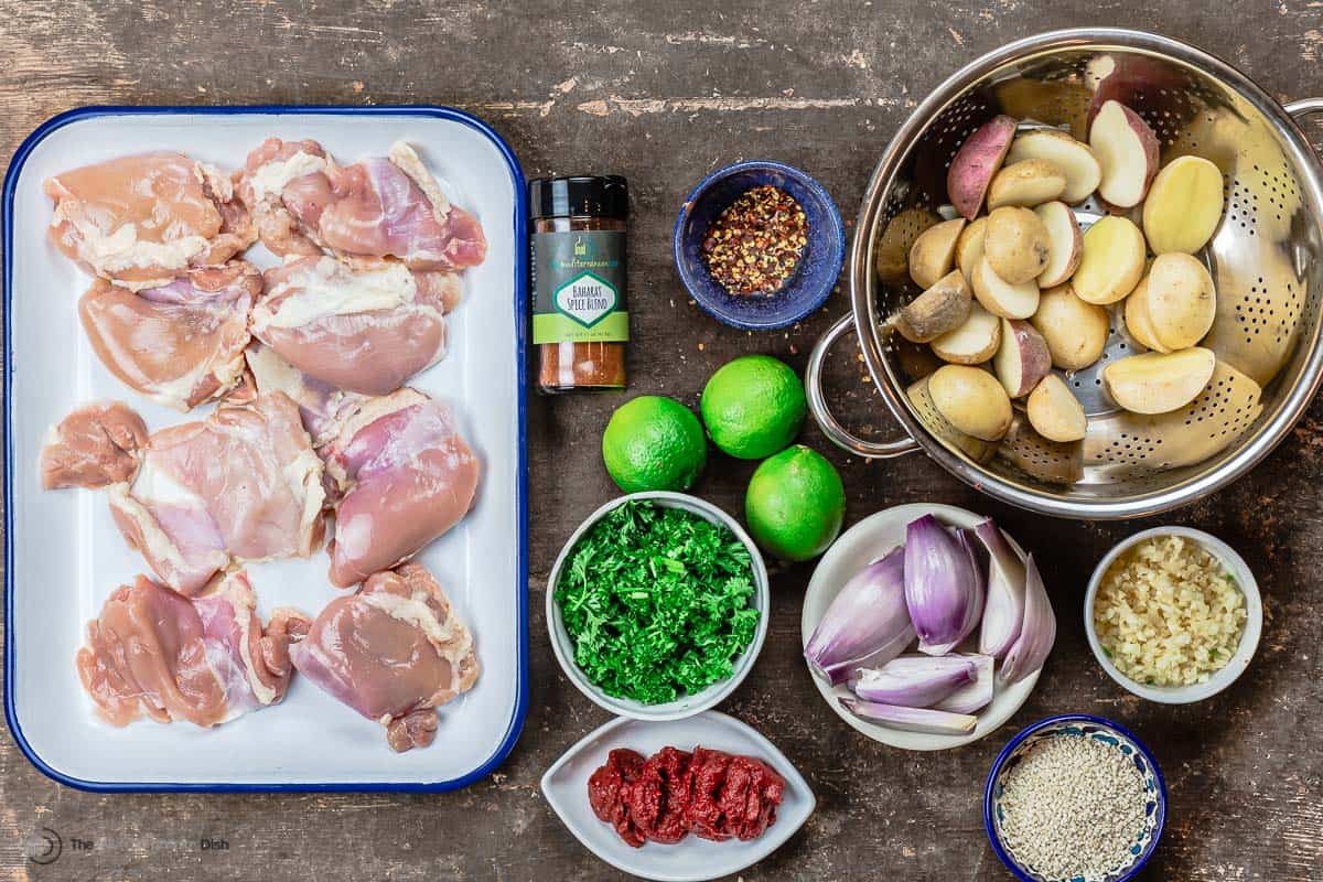 ingredients for baharat chicken including boneless skinless chicken thighs, baharat blend from The Mediterranean Dish, limes, chopped parsley, tomato paste, baby potatoes, shallots, garlic, and sesame seeds