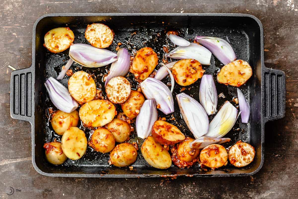Cast-iron baking pan with potatoes and shallots that have been tossed in the baharat marinade