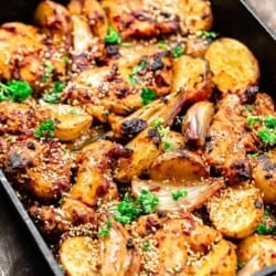 chicken thighs with baharat marinade in a cast-iron baking pan with potatoes and shallots
