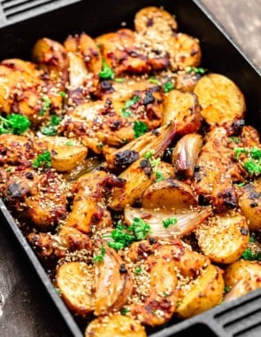 chicken thighs with baharat marinade in a cast-iron baking pan with potatoes and shallots