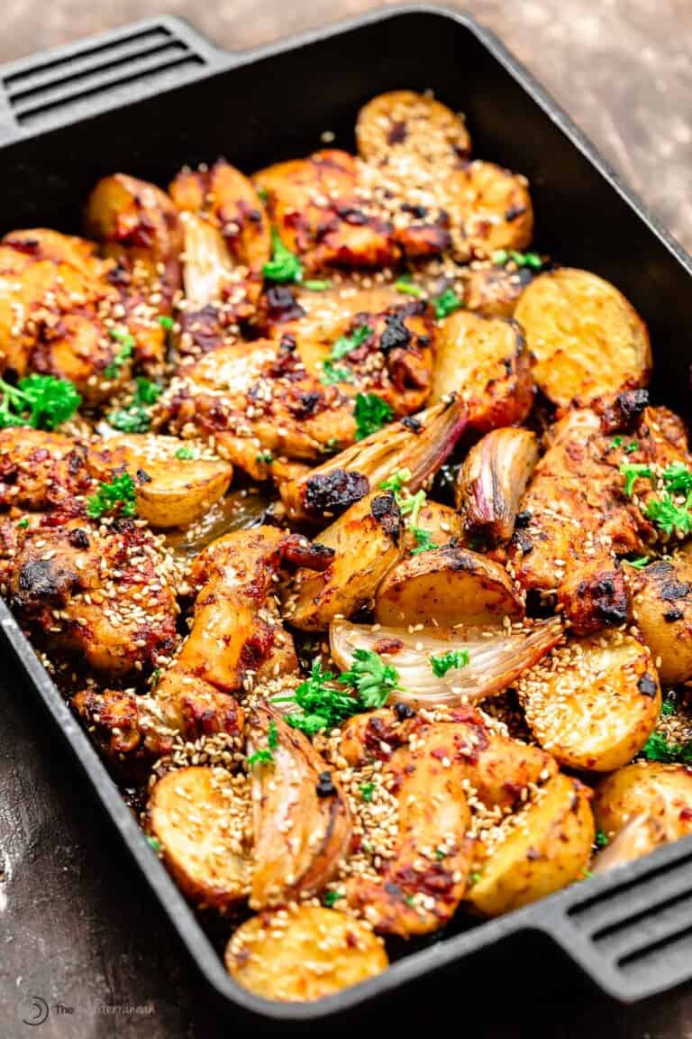 chicken thighs with baharat marinade in a cast-iron baking pan with potatoes and shallots