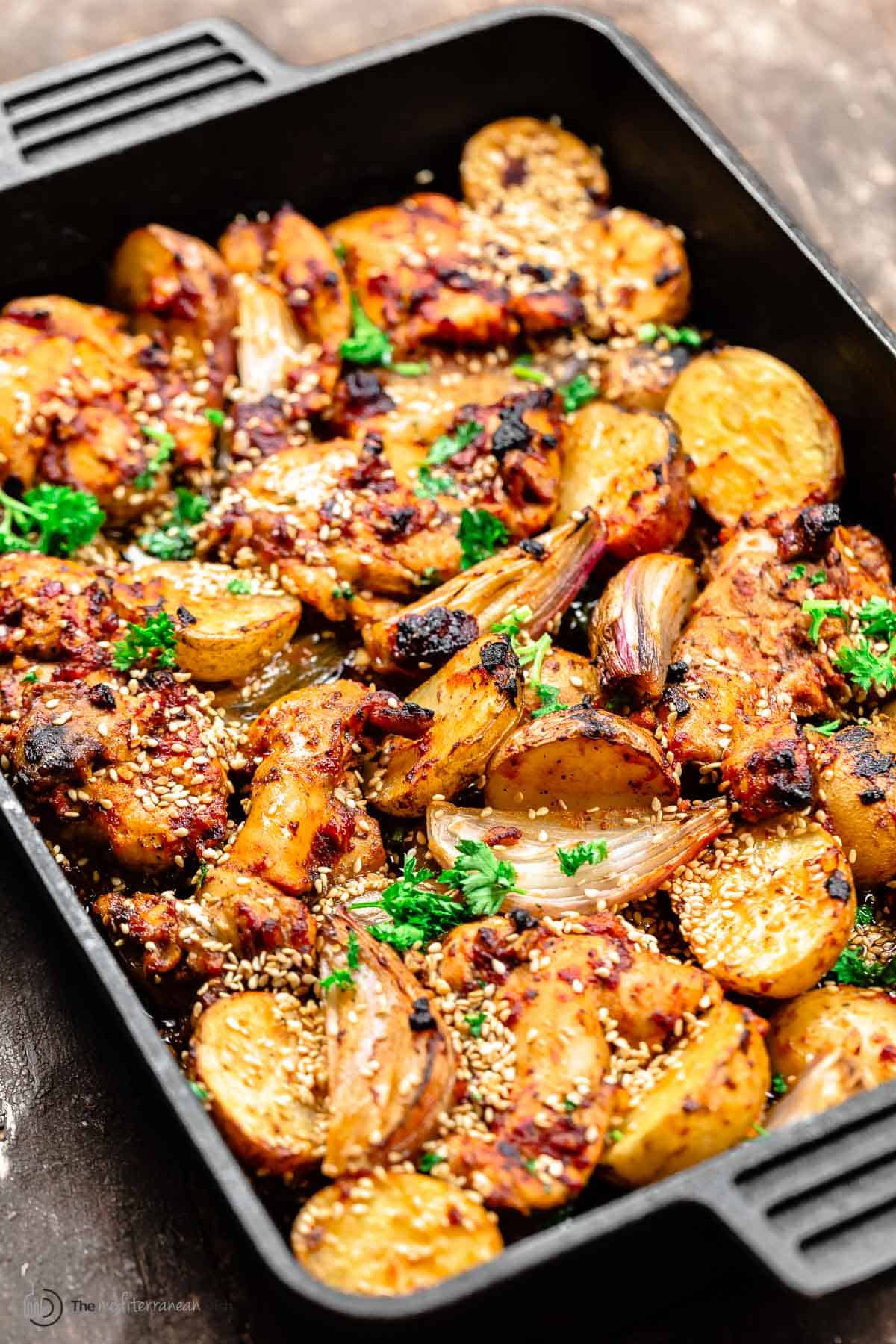 chicken thighs with baharat marinade in a cast-iron baking pan with potatoes and shallots