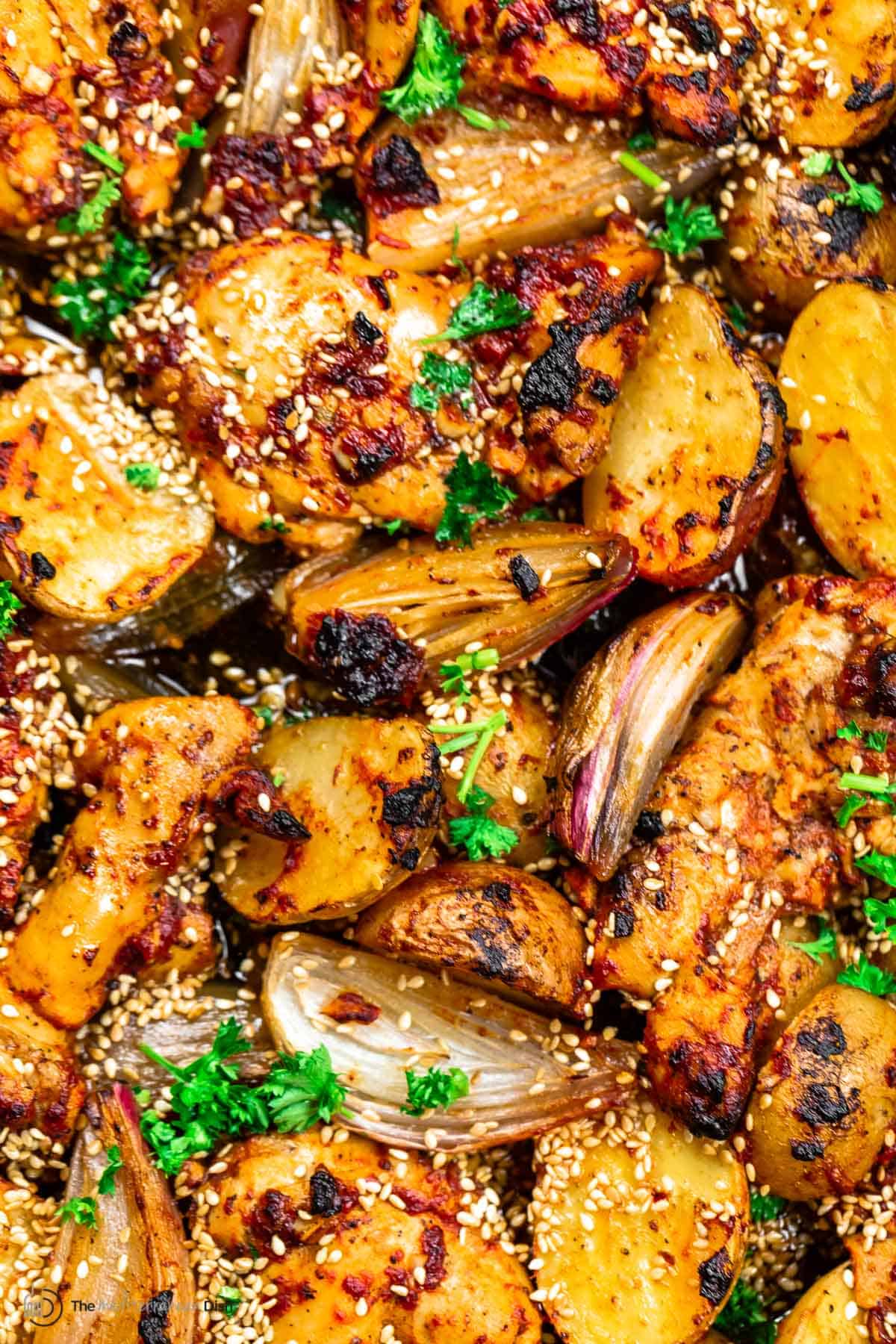 close up of baharat chicken thighs, potatoes, and shallots. Sprinkling of sesame seeds and parsley