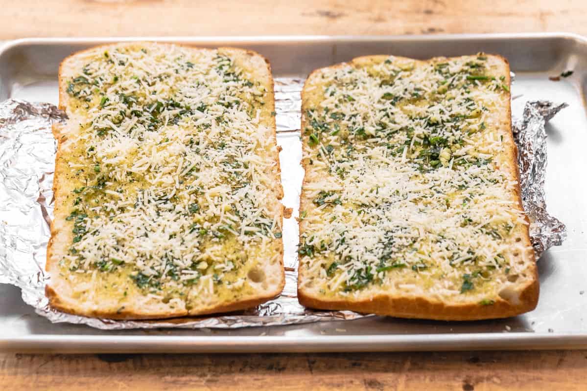 ciabatta halves side by side on a sheet pan with parmesan cheese sprinkled on top