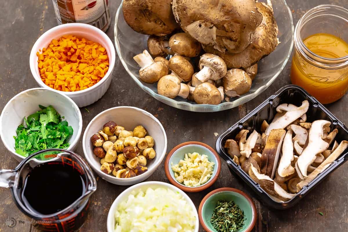 ingredients for mushroom ragu including three kinds of mushrooms, vegetable broth, garlic, onions, herbs, carrots, red wine, and hazelnuts